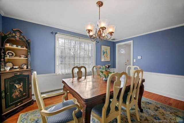 dining space featuring a wainscoted wall, wood finished floors, an inviting chandelier, crown molding, and a baseboard radiator