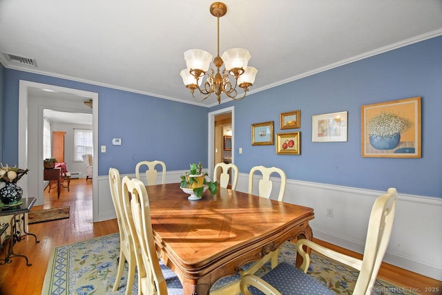 dining space featuring visible vents, crown molding, baseboards, a chandelier, and wood finished floors