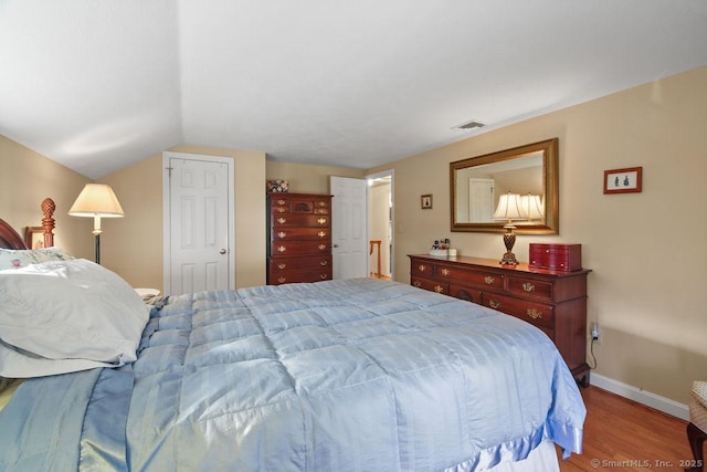 bedroom featuring lofted ceiling, baseboards, visible vents, and light wood-type flooring