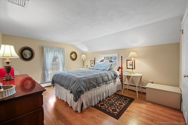 bedroom featuring light wood finished floors, baseboard heating, visible vents, and lofted ceiling