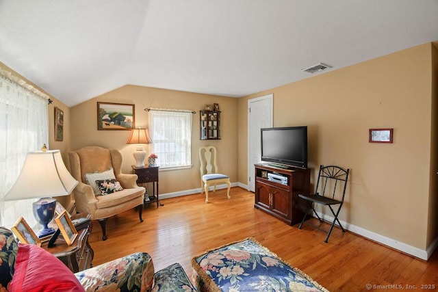 living area featuring visible vents, lofted ceiling, baseboards, and light wood-style flooring