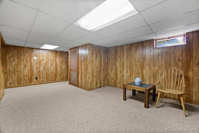 below grade area with a drop ceiling, wooden walls, and carpet