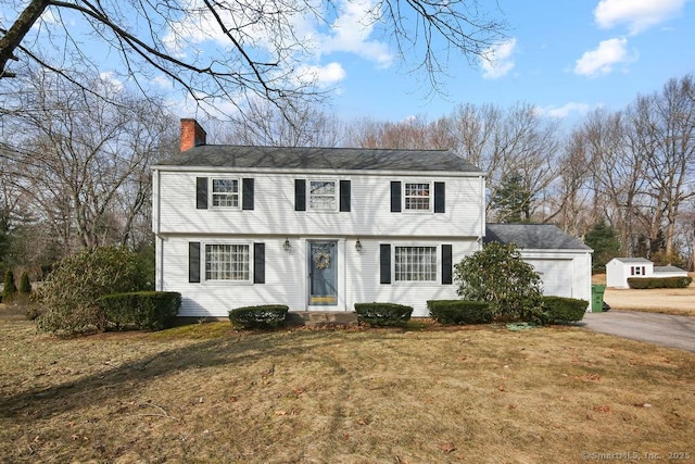 colonial home featuring driveway, a chimney, and a front lawn