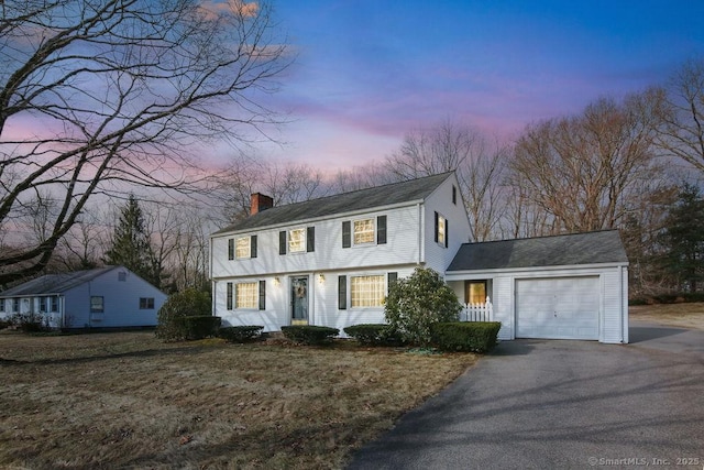 colonial home featuring an attached garage, driveway, and a chimney