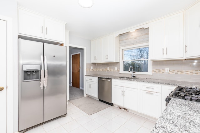 kitchen featuring tasteful backsplash, light stone countertops, stainless steel appliances, white cabinetry, and a sink