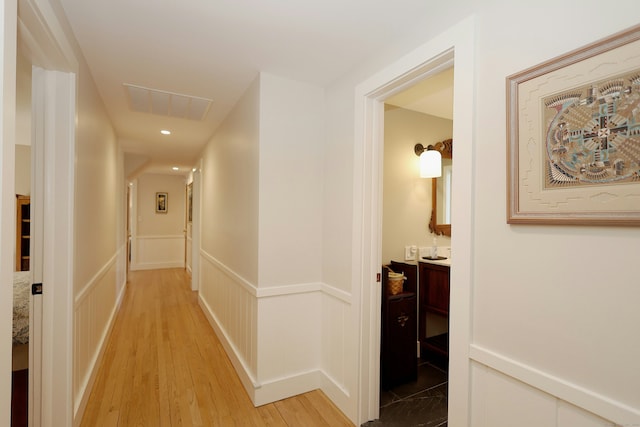 corridor featuring a decorative wall, a wainscoted wall, light wood-type flooring, and visible vents