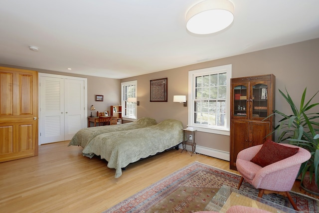 bedroom featuring a baseboard heating unit, baseboards, a closet, and light wood-style flooring