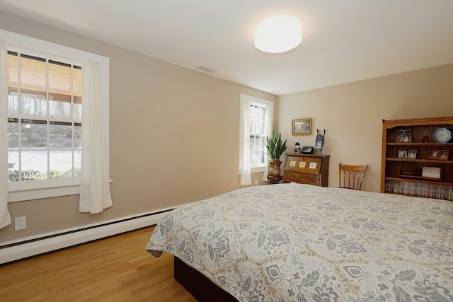 bedroom with light wood-style floors, visible vents, multiple windows, and baseboard heating