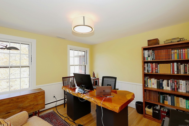 office area with a wainscoted wall, wood finished floors, visible vents, and a baseboard radiator