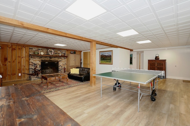 recreation room with a brick fireplace, wood finished floors, baseboards, and wood walls