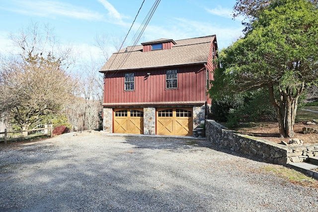 view of side of property with an outbuilding, stone siding, a barn, a detached garage, and a shingled roof