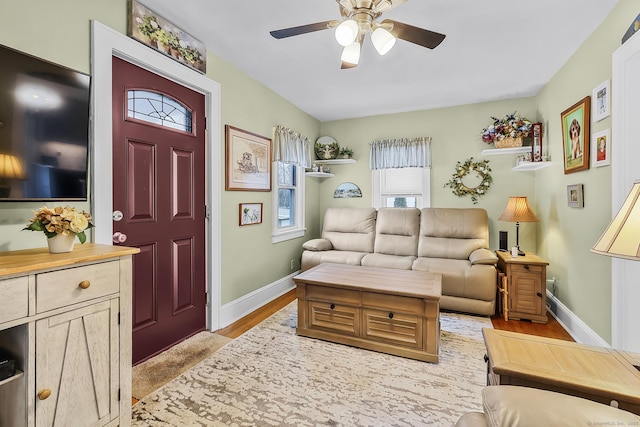 living area featuring a ceiling fan, baseboards, and light wood finished floors