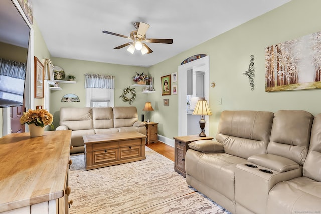 living room with baseboards, a ceiling fan, and light wood-style floors