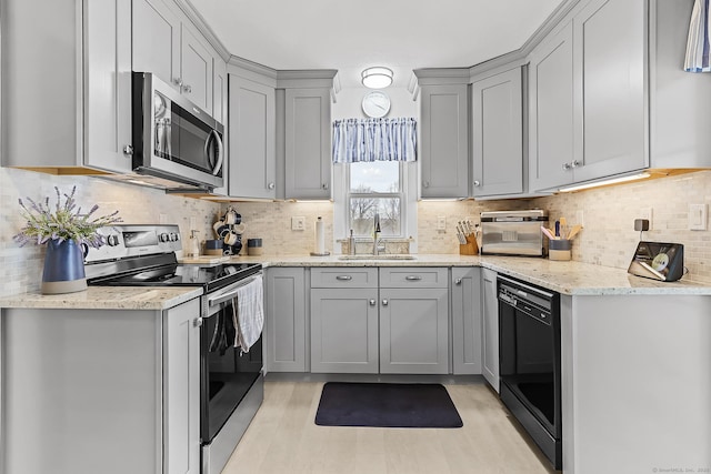 kitchen with light stone countertops, gray cabinetry, a sink, appliances with stainless steel finishes, and tasteful backsplash