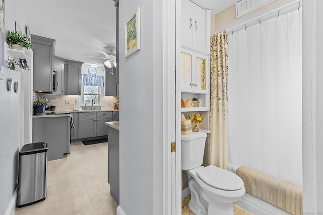 bathroom with toilet, curtained shower, tasteful backsplash, ceiling fan, and vanity