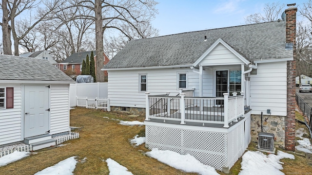 snow covered back of property featuring an outdoor structure, a wooden deck, a fenced backyard, and a chimney