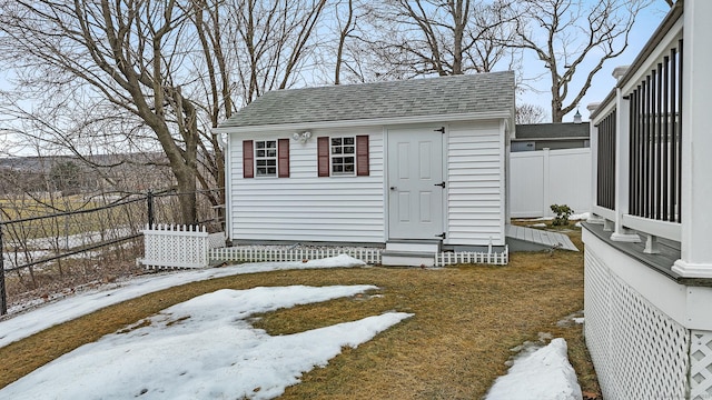 snow covered structure featuring an outbuilding, entry steps, and fence