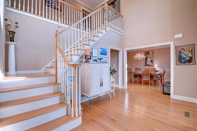 stairs featuring a notable chandelier, baseboards, a high ceiling, and wood finished floors