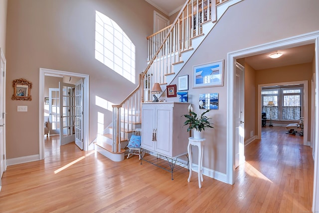 foyer entrance with french doors, stairs, light wood-style floors, and a towering ceiling