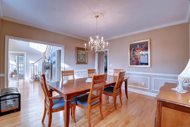 dining area with stairway, light wood finished floors, ornamental molding, wainscoting, and a decorative wall