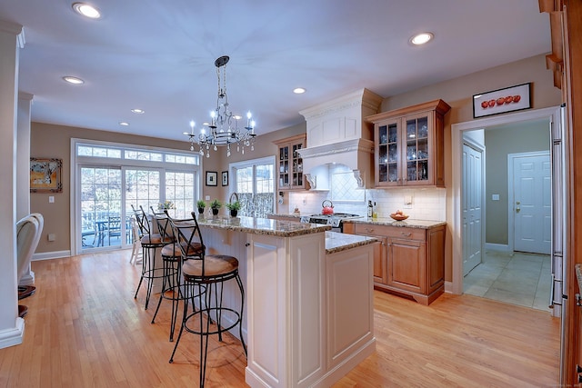 kitchen with a kitchen island, a kitchen bar, decorative backsplash, light wood-style flooring, and stainless steel gas stove