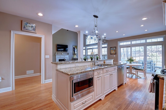 kitchen with light wood finished floors, a kitchen island with sink, stainless steel appliances, a sink, and white cabinetry