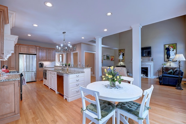 kitchen featuring light stone countertops, a fireplace with flush hearth, a sink, light wood-style floors, and appliances with stainless steel finishes