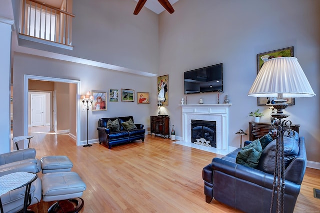 living area with a high ceiling, a fireplace with flush hearth, wood finished floors, and baseboards