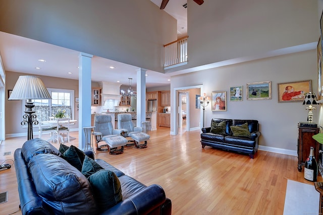 living room with baseboards, light wood-type flooring, recessed lighting, a towering ceiling, and ornate columns