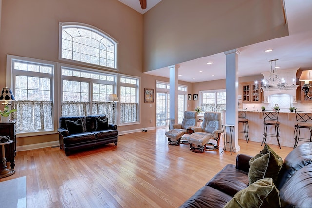 living area featuring decorative columns, baseboards, light wood-style flooring, and a chandelier