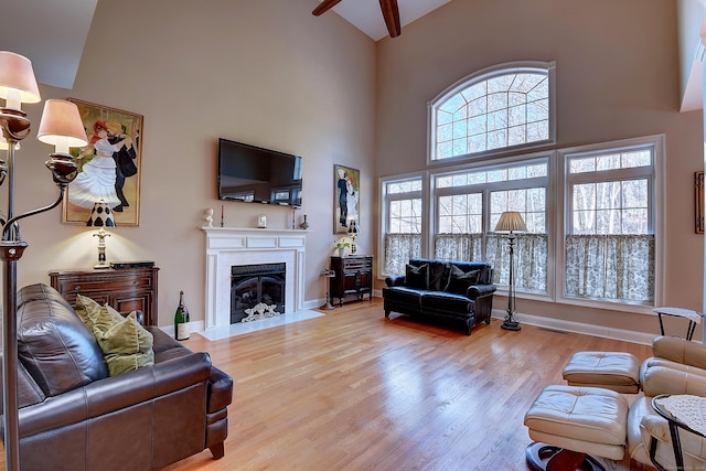 living room featuring visible vents, baseboards, a fireplace with flush hearth, wood finished floors, and high vaulted ceiling