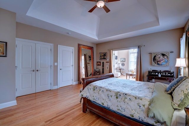 bedroom featuring baseboards, light wood-type flooring, a tray ceiling, and a ceiling fan