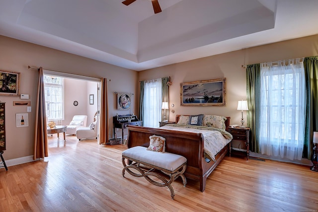 bedroom featuring light wood-type flooring, a raised ceiling, baseboards, and ceiling fan