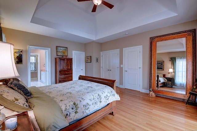 bedroom featuring light wood finished floors, ceiling fan, baseboards, and a tray ceiling