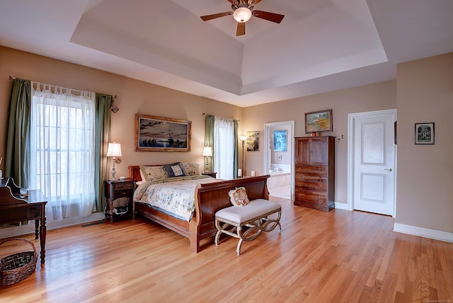 bedroom with light wood-type flooring, a raised ceiling, baseboards, and a ceiling fan