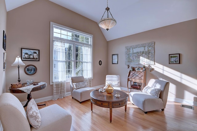 living area with baseboards, lofted ceiling, visible vents, and light wood finished floors