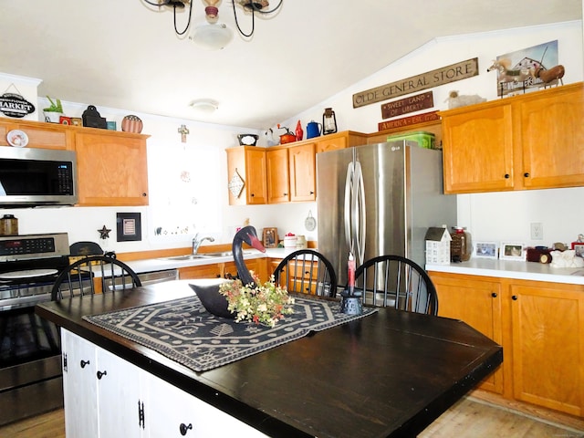 kitchen with a sink, stainless steel appliances, lofted ceiling, and light wood finished floors