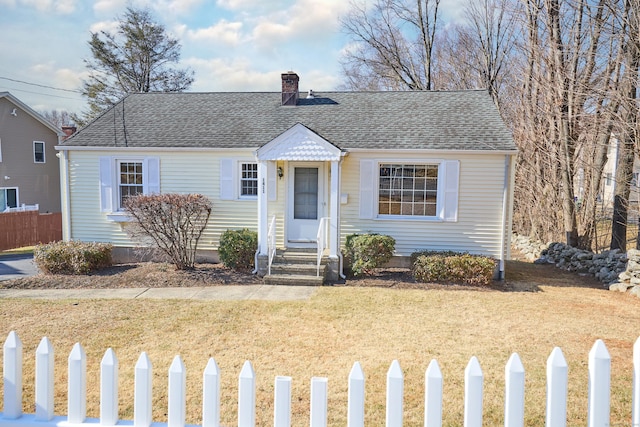 view of front of house featuring a front lawn, roof with shingles, a chimney, and fence