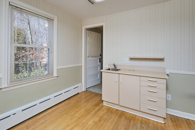 kitchen featuring a baseboard radiator, light countertops, light wood-style floors, white cabinetry, and a sink