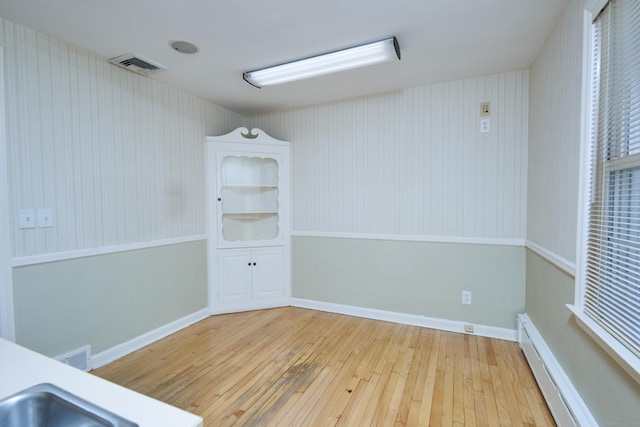 spare room featuring a baseboard heating unit, hardwood / wood-style flooring, baseboards, and visible vents