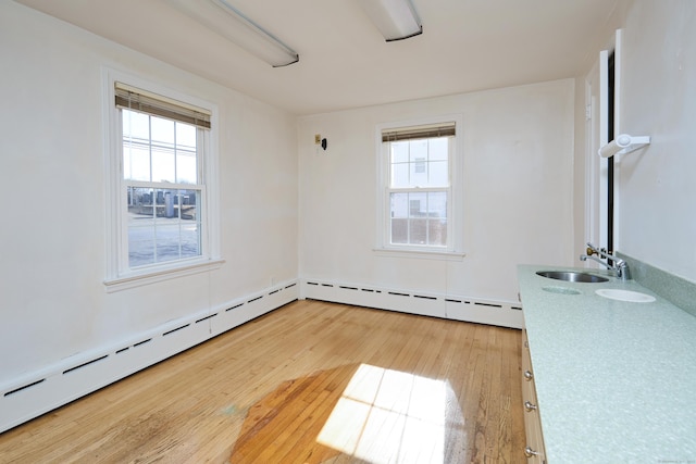 unfurnished room featuring a wealth of natural light, baseboard heating, a sink, and light wood finished floors