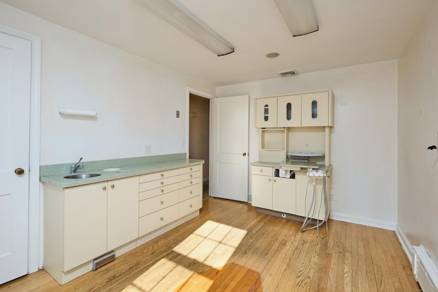 kitchen with light wood finished floors, light countertops, baseboards, and a sink