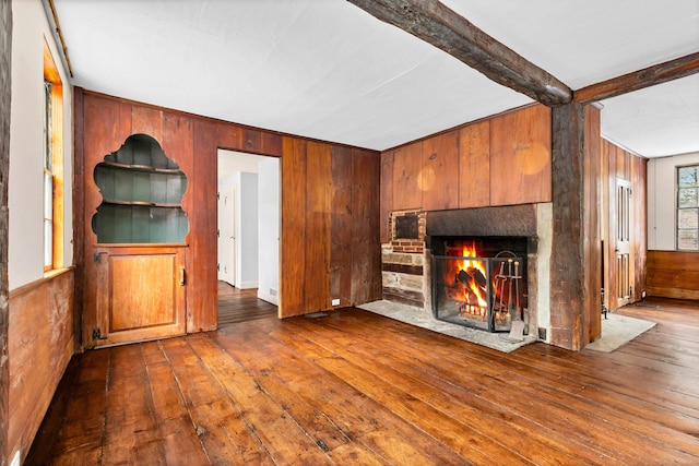 unfurnished living room with hardwood / wood-style floors, beamed ceiling, wood walls, and a fireplace