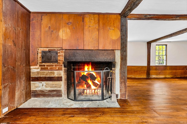 room details featuring wood finished floors, beamed ceiling, a wainscoted wall, wood walls, and a brick fireplace