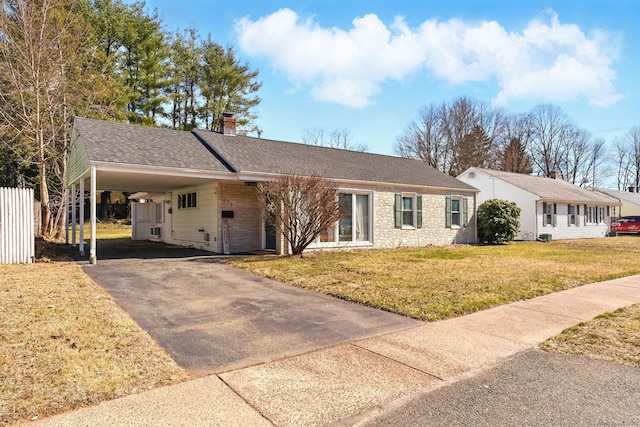 ranch-style house featuring a shingled roof, a front yard, a chimney, a carport, and driveway