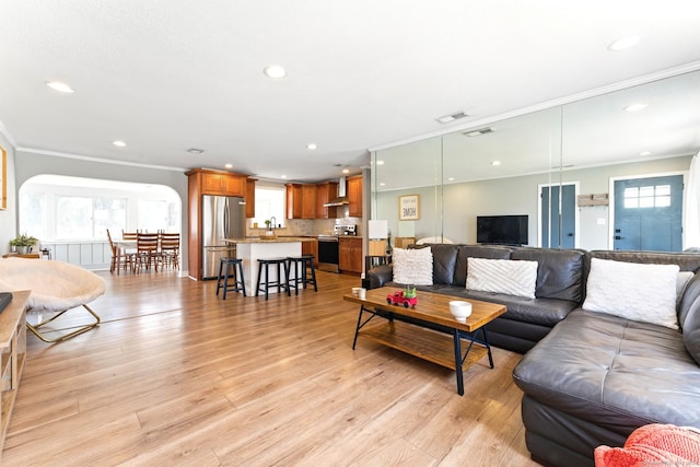 living area with light wood finished floors, a wealth of natural light, and ornamental molding