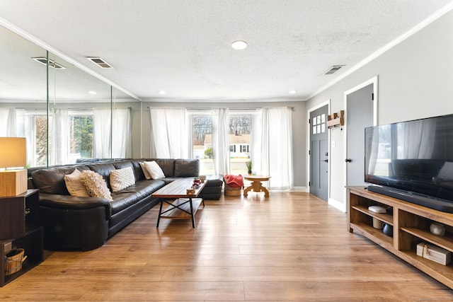 living area featuring wood finished floors, baseboards, visible vents, a textured ceiling, and crown molding