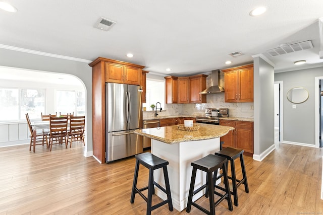 kitchen featuring visible vents, ornamental molding, arched walkways, appliances with stainless steel finishes, and wall chimney exhaust hood