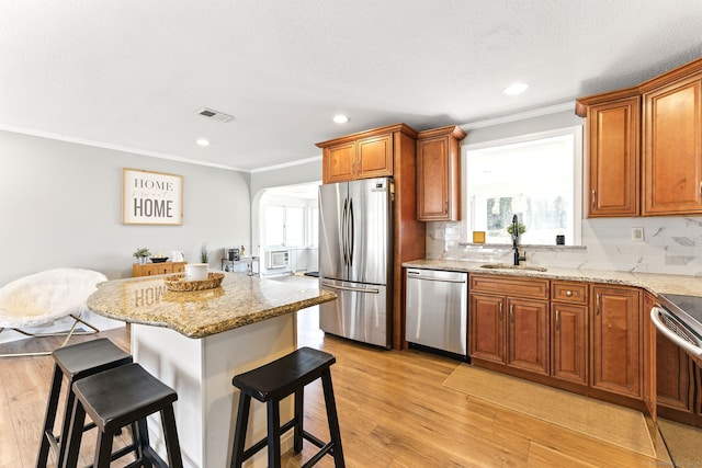 kitchen with visible vents, a kitchen bar, light wood-style flooring, stainless steel appliances, and a sink