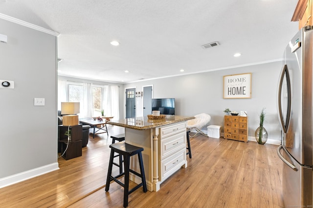 kitchen featuring crown molding, a breakfast bar area, visible vents, and freestanding refrigerator